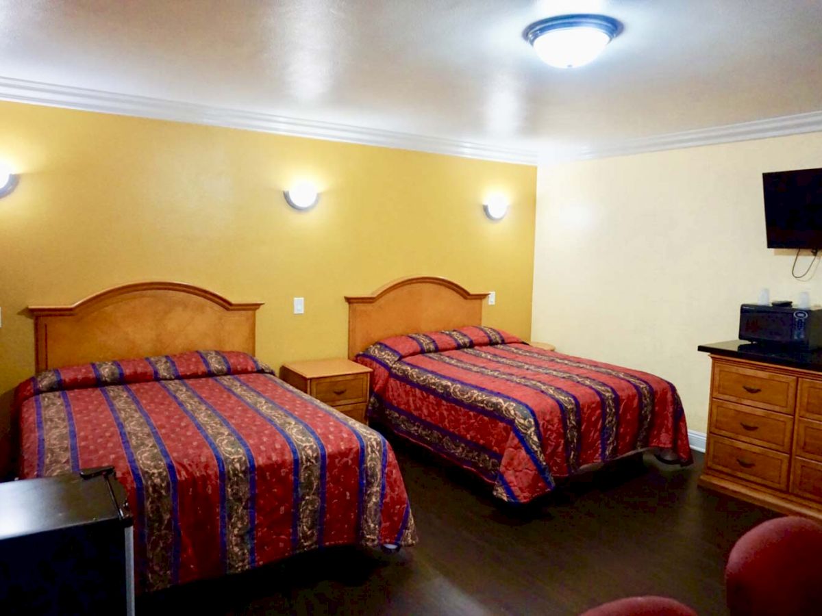 The image shows a hotel room with two double beds, a TV mounted on the wall, a dresser, and nightstands, all with warm lighting.