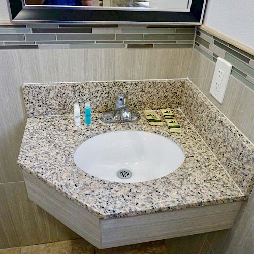 A small bathroom sink with granite countertop, a faucet, and several small toiletry items neatly arranged beside the sink.