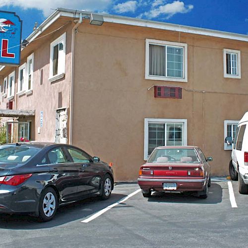 The image shows the exterior of The Patio Motel with parked cars and a van in the lot, under a clear sky with scattered clouds.