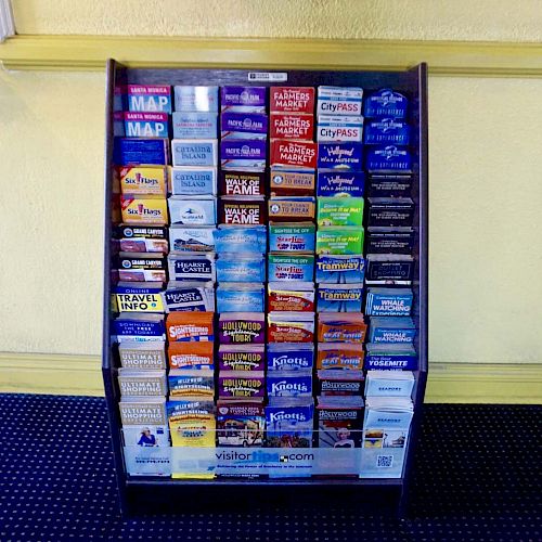 The image shows a rack with various brochures, maps, and information pamphlets for tourists, likely located in a lobby or visitor center.