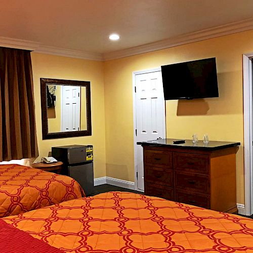 A hotel room with two neatly made beds, a wall-mounted TV, a dresser, a small fridge, a mirror, and an open door to a closet area.