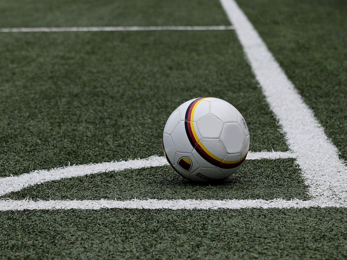 A soccer ball is placed at the corner of a green soccer field, near the white boundary lines.