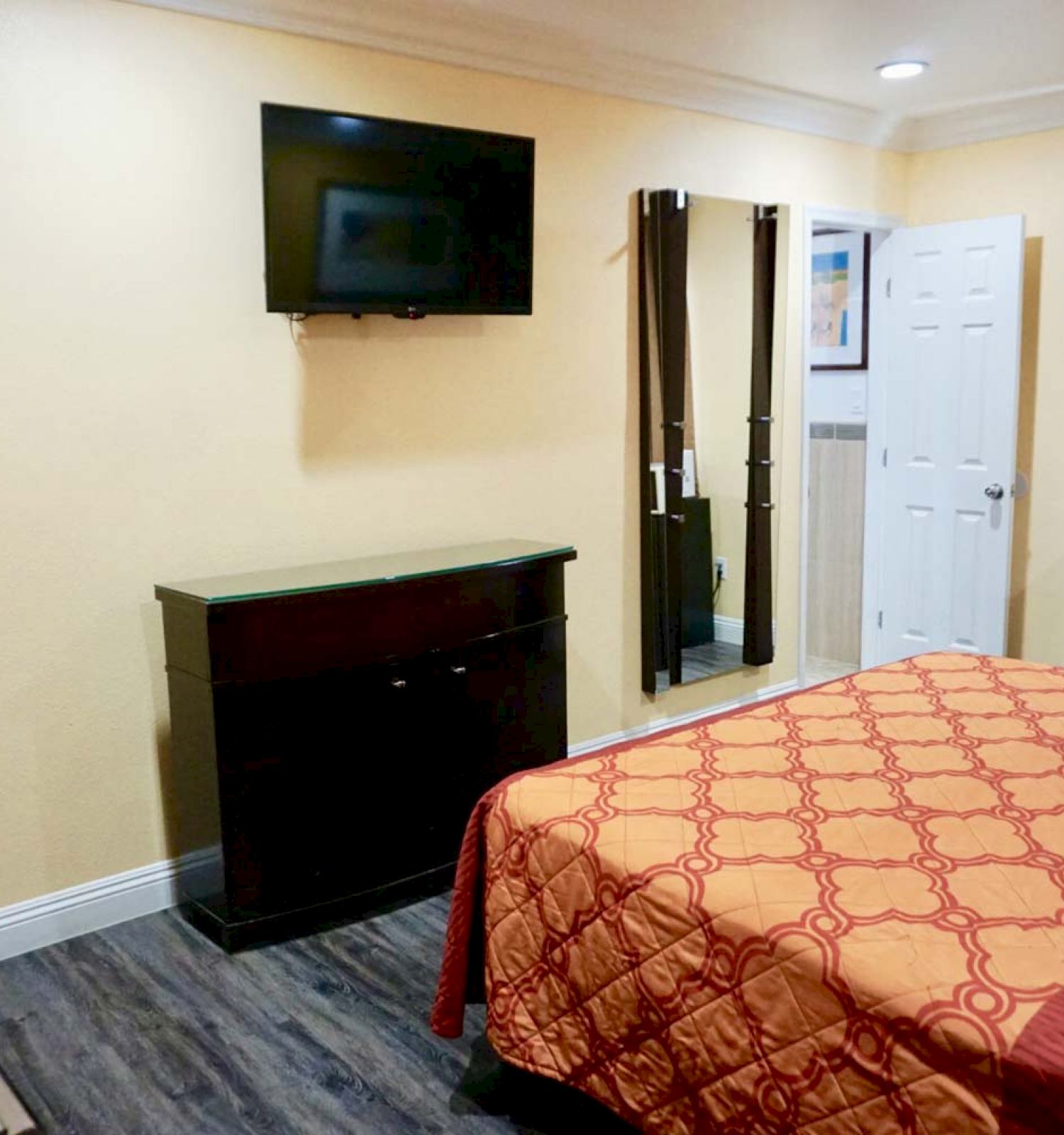 A neatly furnished hotel room with a bed, TV, dresser, microwave, and mirror. There is also a desk with a chair near the bed.