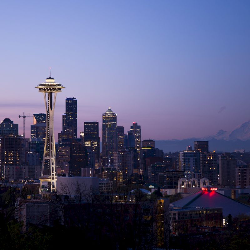 The image shows a city skyline with a prominent tower and mountainous background, taken at dusk.