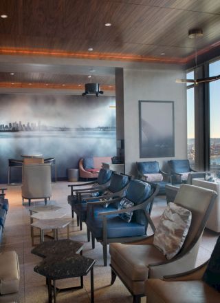 A modern lounge area with comfortable seating, large windows providing a scenic view of a city skyline and waterfront, and contemporary decor.