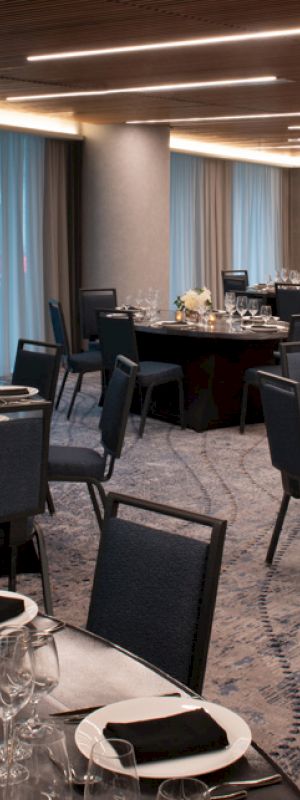 A modern dining venue with round tables set for a formal event, including place settings, glassware, candles, and floral centerpieces.