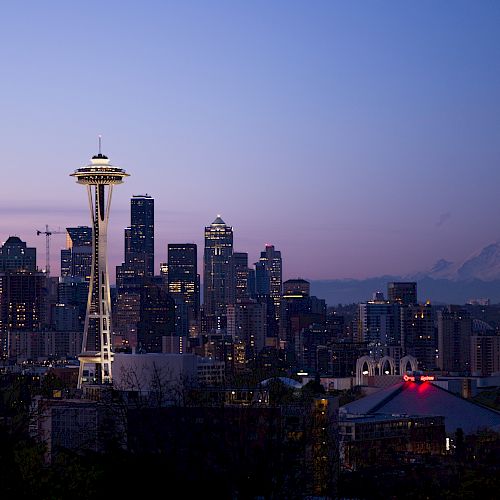 A view of the Seattle skyline at dusk, featuring the Space Needle and Mount Rainier in the background against a twilight sky.